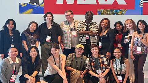 A group of 15 standing in front of a red sign with text in white letters, MAX, at The Digital Edge Awards winners, Adobe Max 2024.
